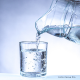 Wasser wird mittels einer Glaskaraffe in ein Wasserglas geschüttet