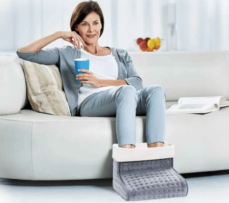 Alltagshilfen gegen kalte Füße - der Promed Fußwärmer, getragen von einer sympathischen Bestagerin, die Tee auf dem Sofa trinkt