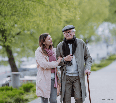 Alltagshilfen in Anwendung - Senior mit Gehstock beim Spaziergang mit junger Frau (Tochter)