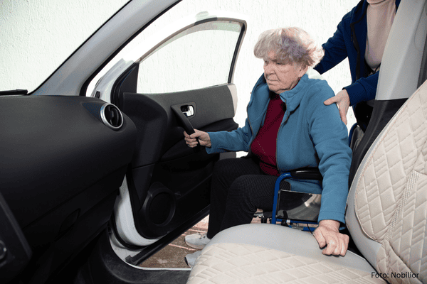 Seniorin wir vom Rollstuhl ins Auto geholfen - Gehilfe