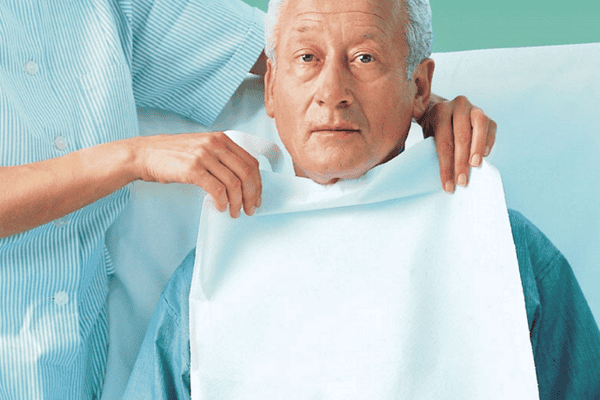 Lätzchen für Erwachsene - Einweg wird einem Senior durch die Pflegerin / Krankenschwester umgezogen