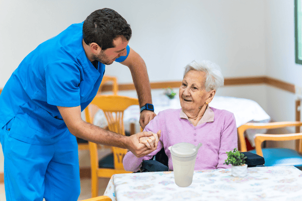 Alte Dame mit Pfleger - Trinkhilfe steht auf dem Tisch